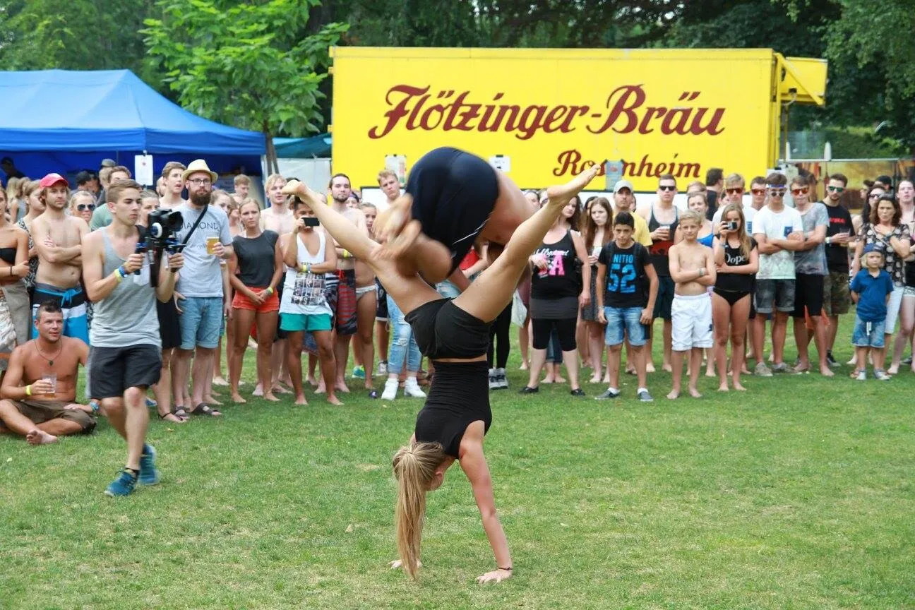 Ein Athlet im Handstand vor dem Festivalpublikum, dahinter der gelbe Lastwagen der Bühne.