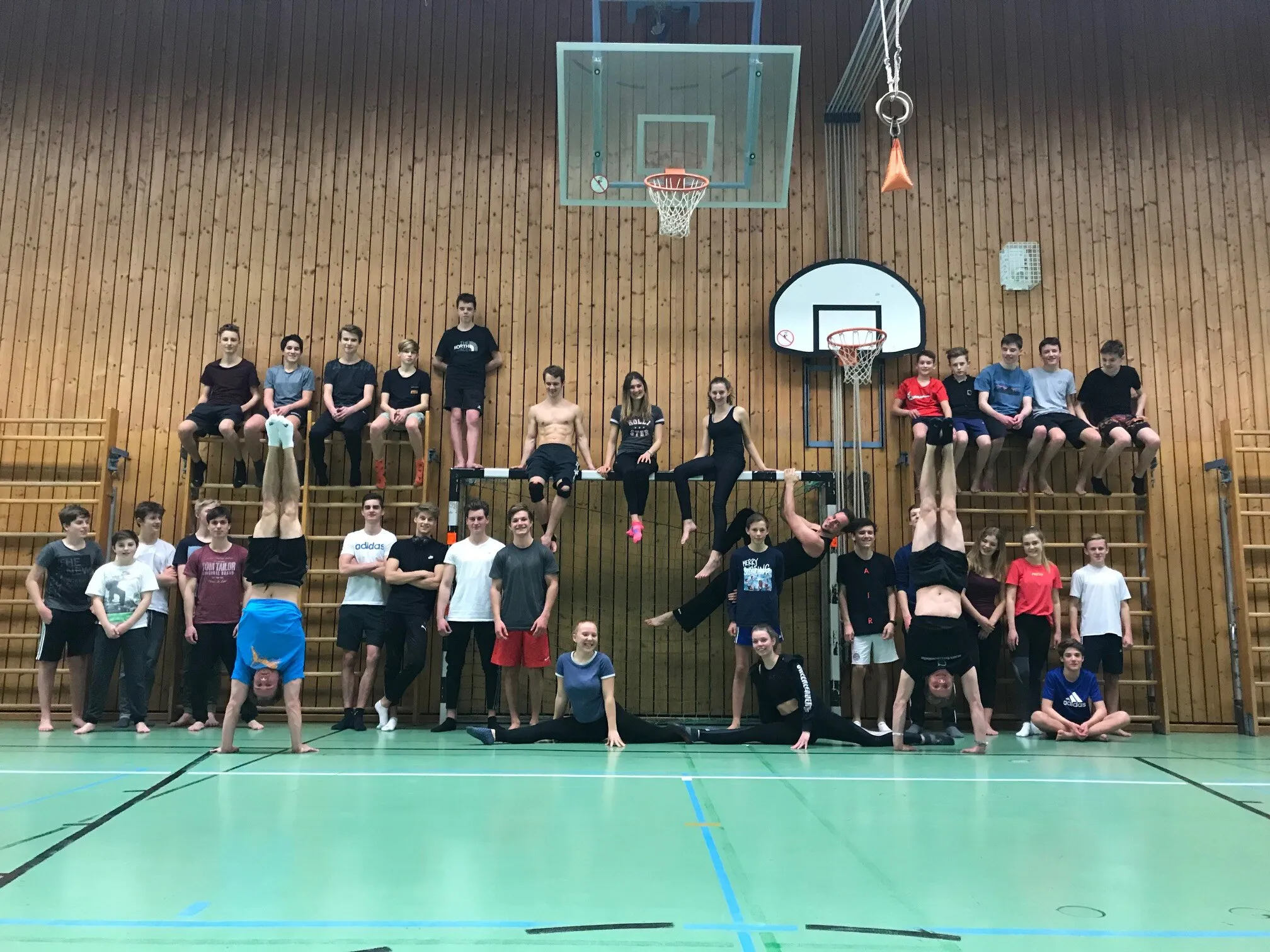 Das Kolbermoorer Team an und auf der Sprossenwand, viele in Handstand und Spagat, auf mintgrünem Hallenboden.